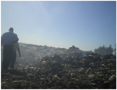 Two men climbing up a hill composed of rubble and trash.