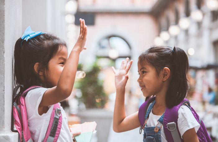 Two young girls with their backpacks up high fiving.