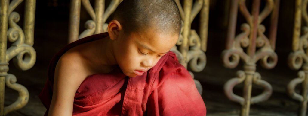 A young Buddhist boy in red studying scriptures